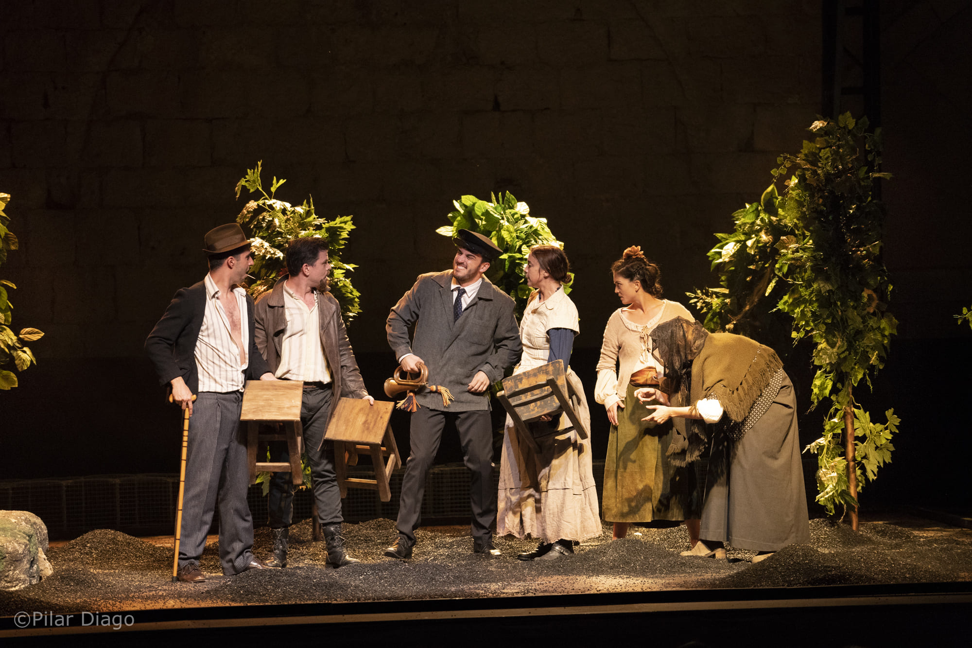 Actors on stage. They all are listening to a man carrying a horn. 