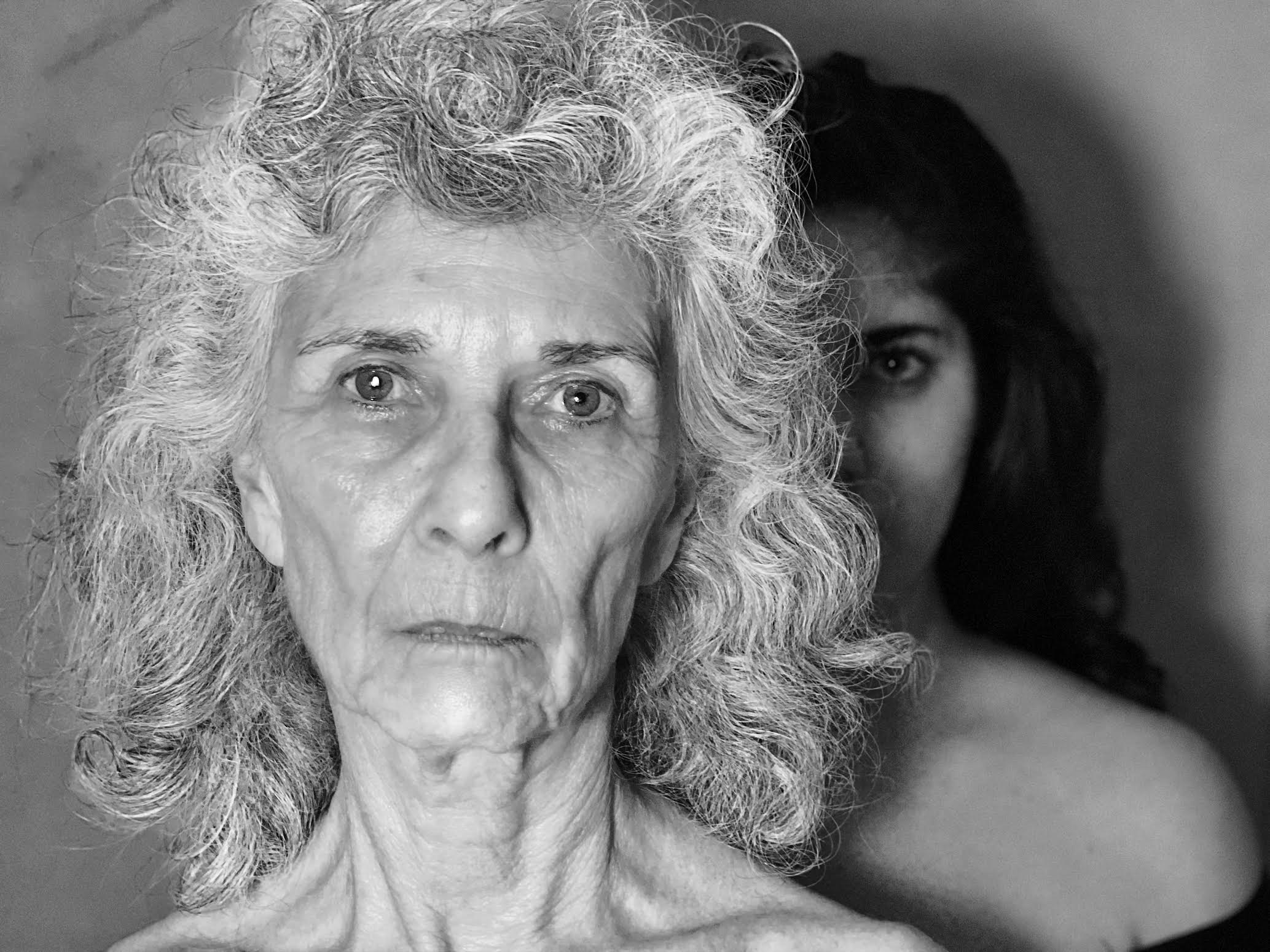 Image of an older woman staring into the camera and a younger woman staring behind her.