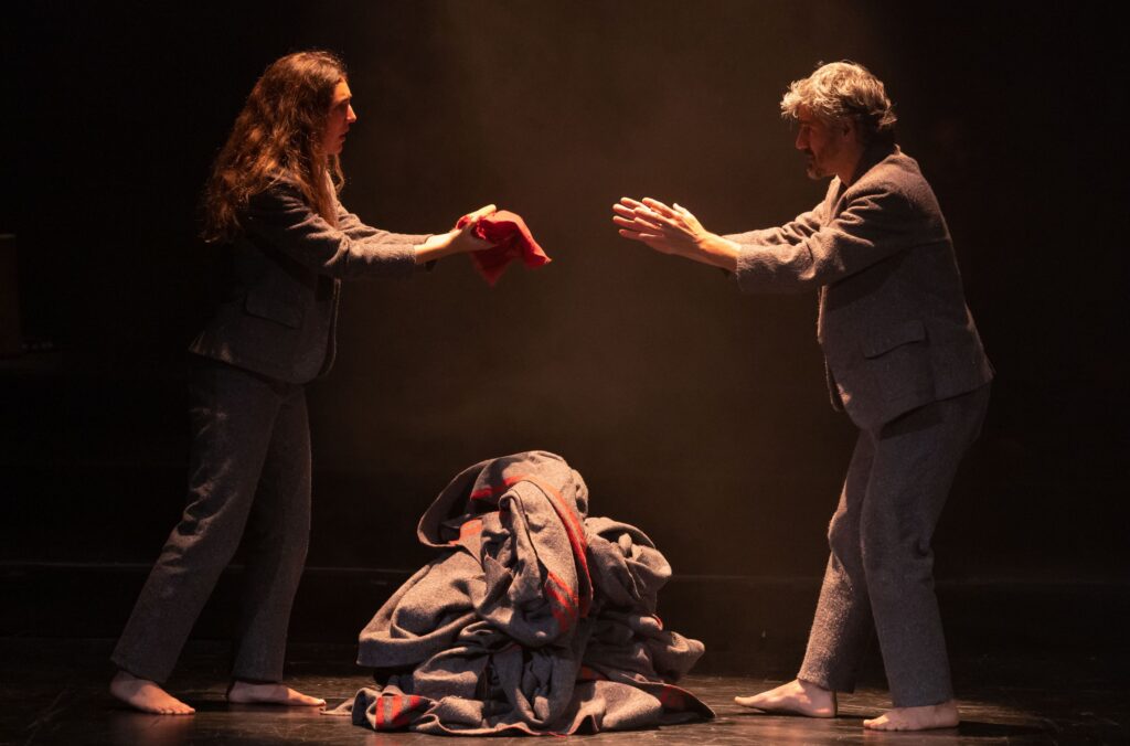 Two actors reaching towards each other on stage