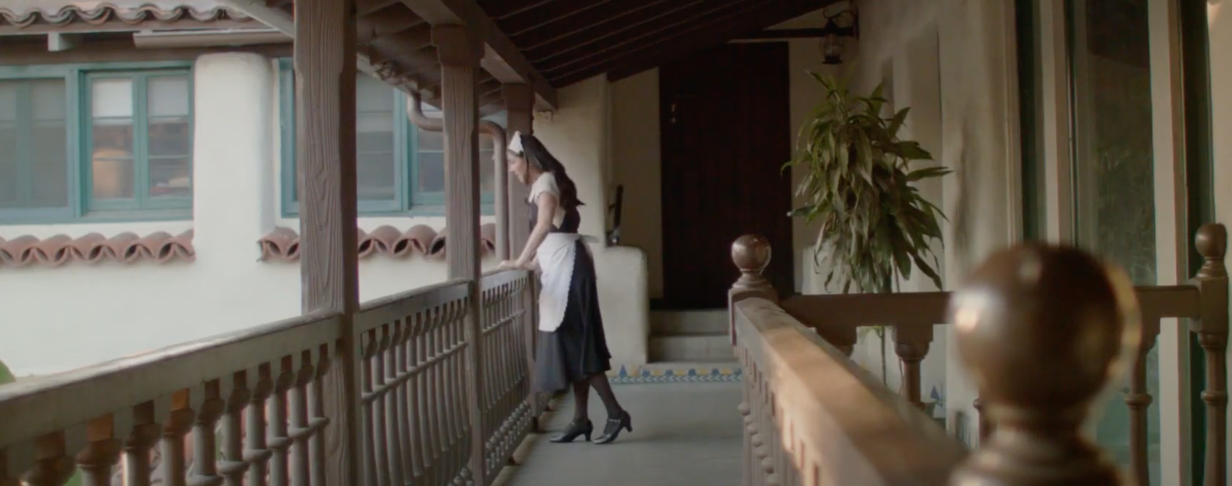 Photo of a woman who is dressed as a maid and looking over the balcony. 