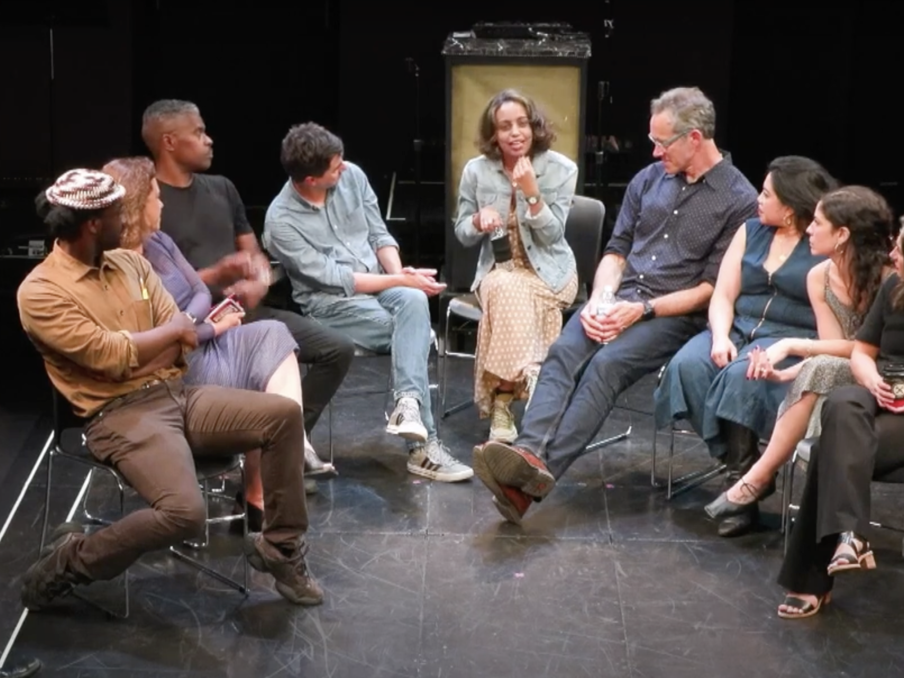 Click here to watch recordings of talks. The image is of people having a discussion on a theater stage. 