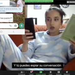 A woman in a Zoom meeting with her phone on one hand and a book in the other.