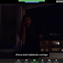 A Zoom meeting with a girl in the dark. The caption reads "ahora esta hablando contigo"