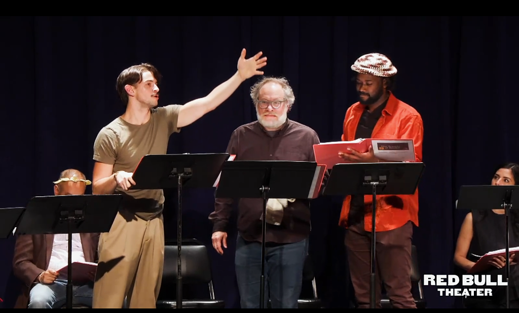 photo of the interior of a black box theater with one actor in the middle of a speech while two others look on
